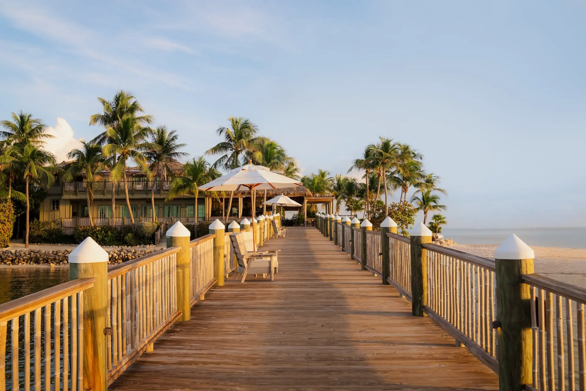 A boardwalk at sunset with lounge chairs and umbrellas at Little Palm Island