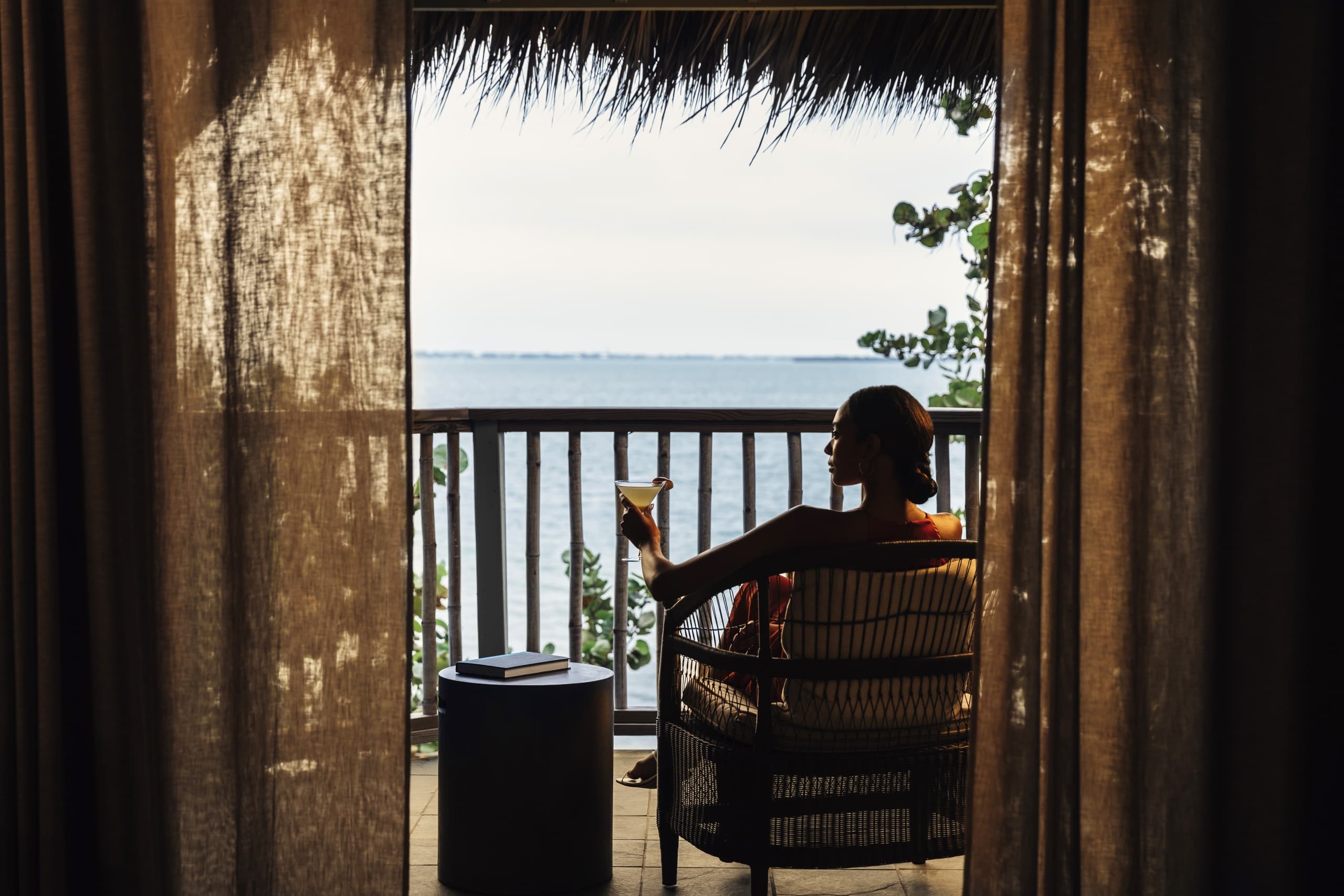 A woman drinking a cocktail on her oceanfront terrace at Little Palm Island Resort.