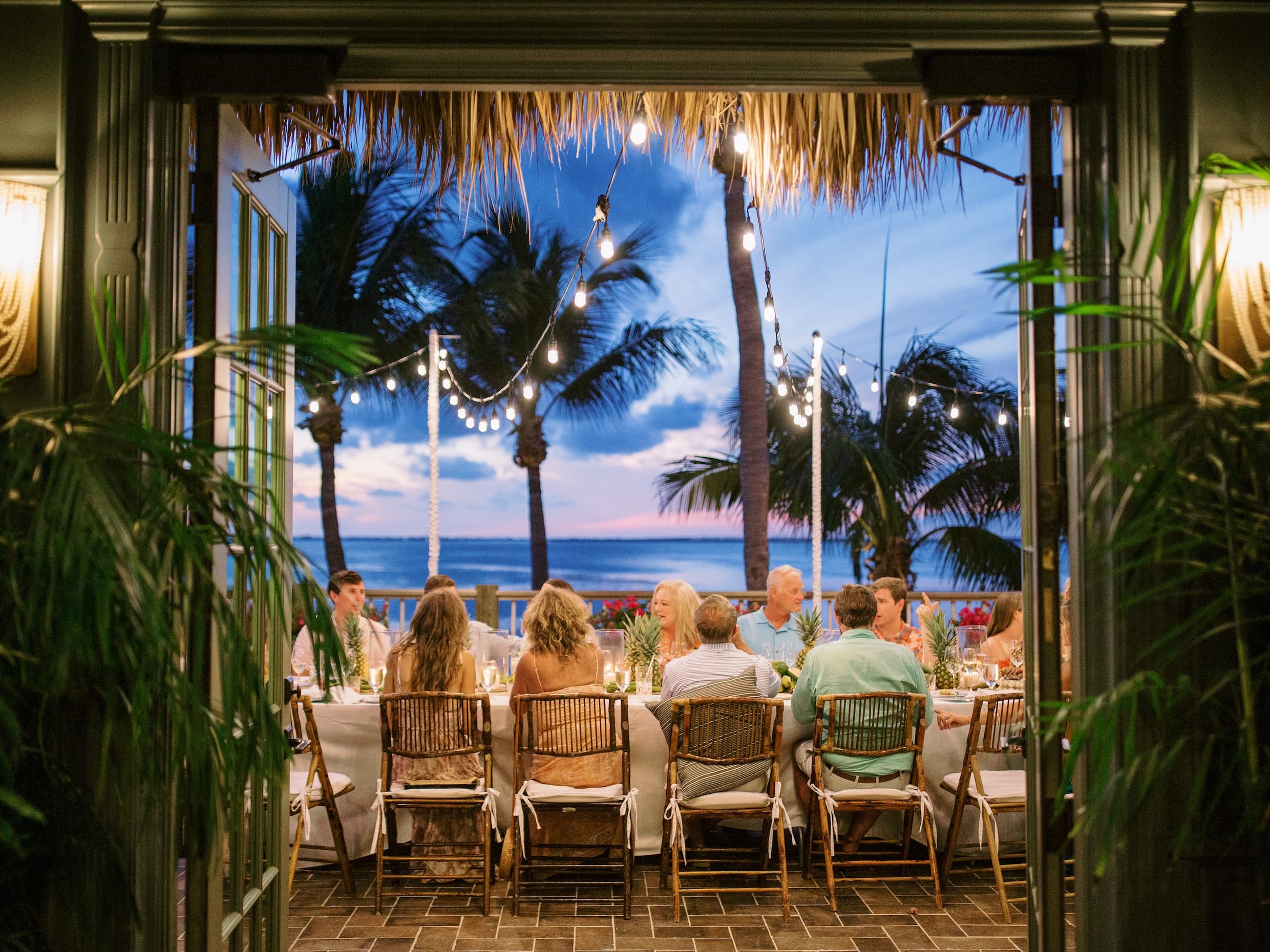 A large guest group seated at a banquet style table, sharing a meal at night on the patio of Little Palm Island
